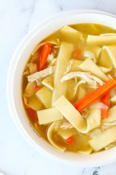 a white bowl filled with chicken noodle soup on top of a marble countertop