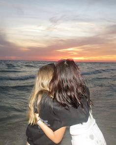 two women hugging each other on the beach at sunset or sunrise with waves coming in from the ocean