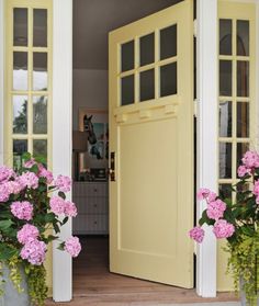 two flower pots with pink flowers in front of a yellow door and some white pillars