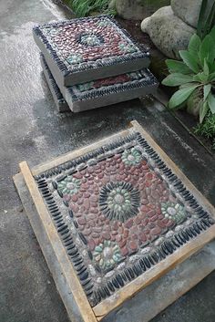 two square mosaics sitting on the ground next to each other in front of some plants