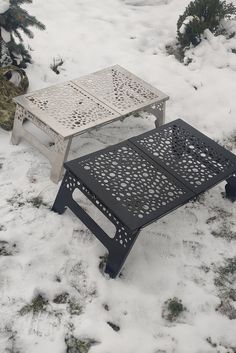 a metal table sitting in the snow next to a pine tree with no leaves on it