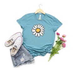 a t - shirt with a flower on it next to some flowers and shoes,