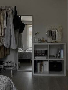 a room with a bed, bookshelf and clothes hanging on the rack in it