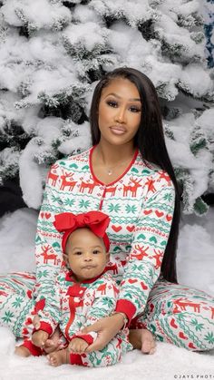 a woman and her baby wearing christmas pajamas sitting in front of a tree with snow on the ground