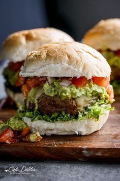 two burgers with meat, lettuce and tomato on a cutting board next to each other