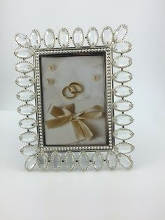 an ornate frame with two wedding rings and pearls on it, as well as a bow