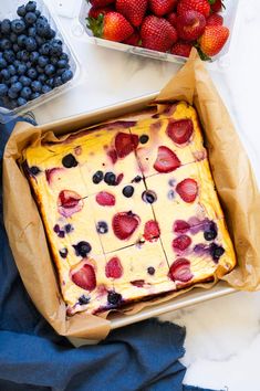 a cake in a box with strawberries and blueberries next to it on a table