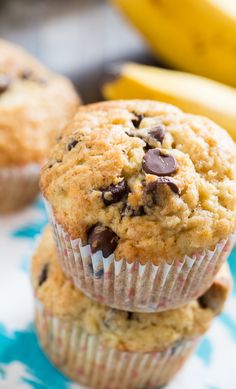 two banana muffins stacked on top of each other with chocolate chips and bananas in the background