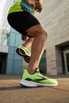 a man in black shorts and neon green shoes is running on the pavement near a building