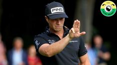 a man in black shirt and hat holding his hand up to the air while playing golf