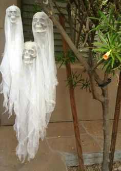 two skeletons in white ghost costumes hanging from a tree