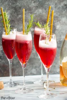 three wine glasses filled with red liquid and garnished with rosemary