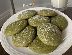 green cookies on a white plate next to a glass of milk