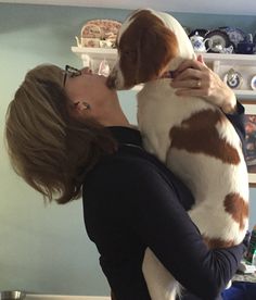 a woman holding a dog in her arms and kissing it's face with both hands