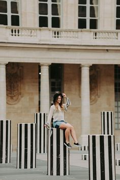 a woman sitting on top of two black and white poles in front of a building