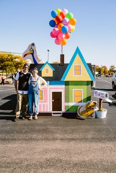 two people standing in front of a house made out of cardboard boxes with balloons on top