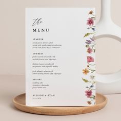 the menu card is next to a white vase with pink flowers and greenery on it