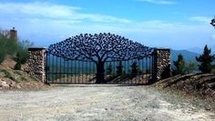 an iron gate with a tree on top and mountains in the background, surrounded by stone pillars