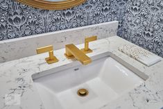 a bathroom sink with marble counter top and gold faucet