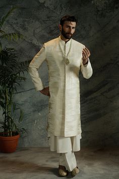 An ivory white closed sherwani detailed with a hidden placket and sloped band, adorned with textured chevron pattern embroidery in shades of gold and ivory white.

Fabric: Jamawar
Color: Ivory White