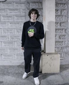 a young man standing next to a white brick wall