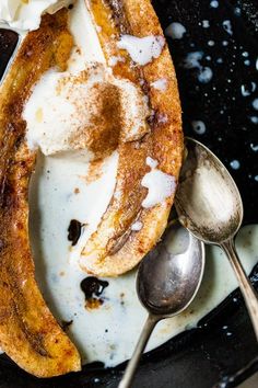 a black plate topped with bananas and whipped cream next to spoons on top of it