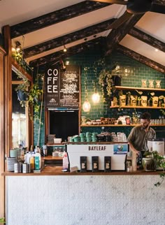 a man standing behind a counter in a restaurant with lots of plants on the shelves