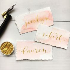 three pieces of watercolor paper with gold foil lettering on them next to a fountain pen