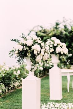 three white vases with flowers on them are sitting in the grass near some benches