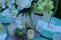 the table is set with white and green flowers in vases, candles, and place settings