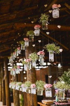 mason jars filled with flowers and greenery are hung from the rafters in this rustic barn wedding