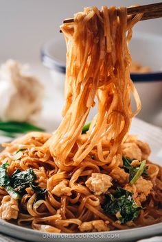 noodles being lifted from a plate with chopsticks over them and sauce on the side