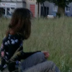 a woman sitting on the ground in front of a building with a dog looking at her