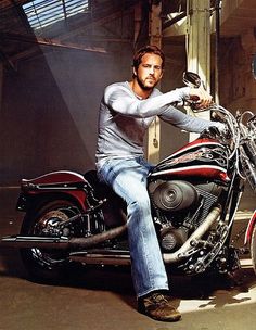 black and white photograph of a man sitting on a motorcycle with his hand on the handlebars