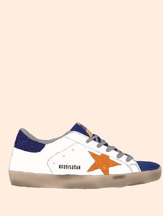 a white and blue sneaker with an orange star on the side, against a pink background