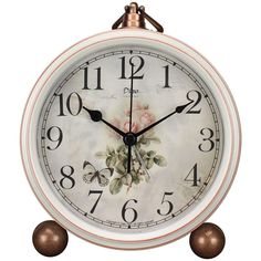 a white clock with flowers on the face and two brown balls in front of it