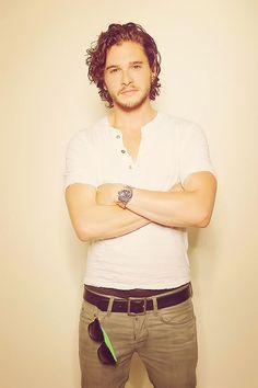 a man with his arms crossed standing in front of a white wall and looking at the camera