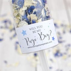 blue and white confetti in a glass vase with a sign that says will you be my page boy?