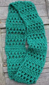 a green crocheted scarf laying on top of a wooden table