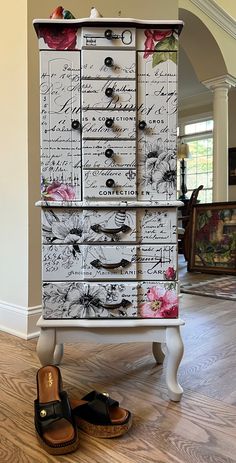 a pair of shoes sitting on top of a white cabinet with drawers and flowers painted on it