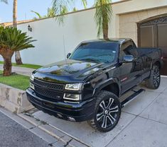 a black truck is parked in front of a house with palm trees on the sidewalk