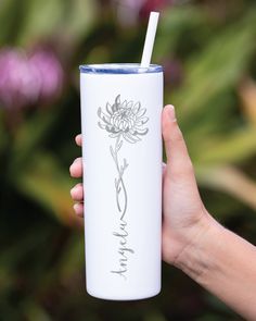 a hand holding a white tumbler cup with a flower on the side and a straw in it