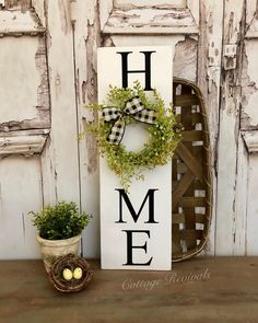 a sign that says home with a wreath and potted plant