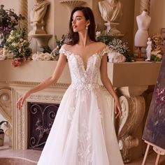 a woman standing in front of a fireplace wearing a wedding dress with flowers on it