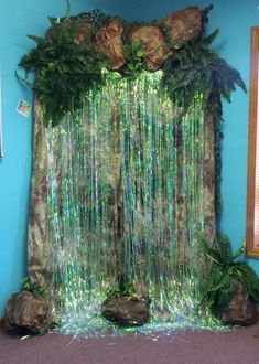 an artificial waterfall made out of plants and rocks in a blue room with green walls