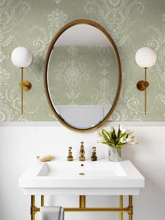 a white sink sitting under a mirror next to a gold faucet and wall mounted light