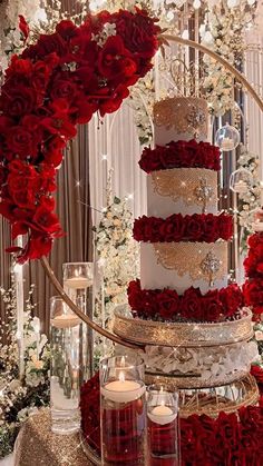 a wedding cake with red roses and candles in front of a chandelier filled with flowers