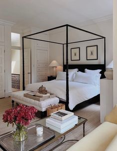 a bedroom with a four post bed and white walls, carpeted flooring and furniture