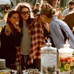 two women standing next to each other at a table with food and drinks on it