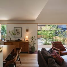 a living room filled with furniture next to a wooden table and window covered in plants